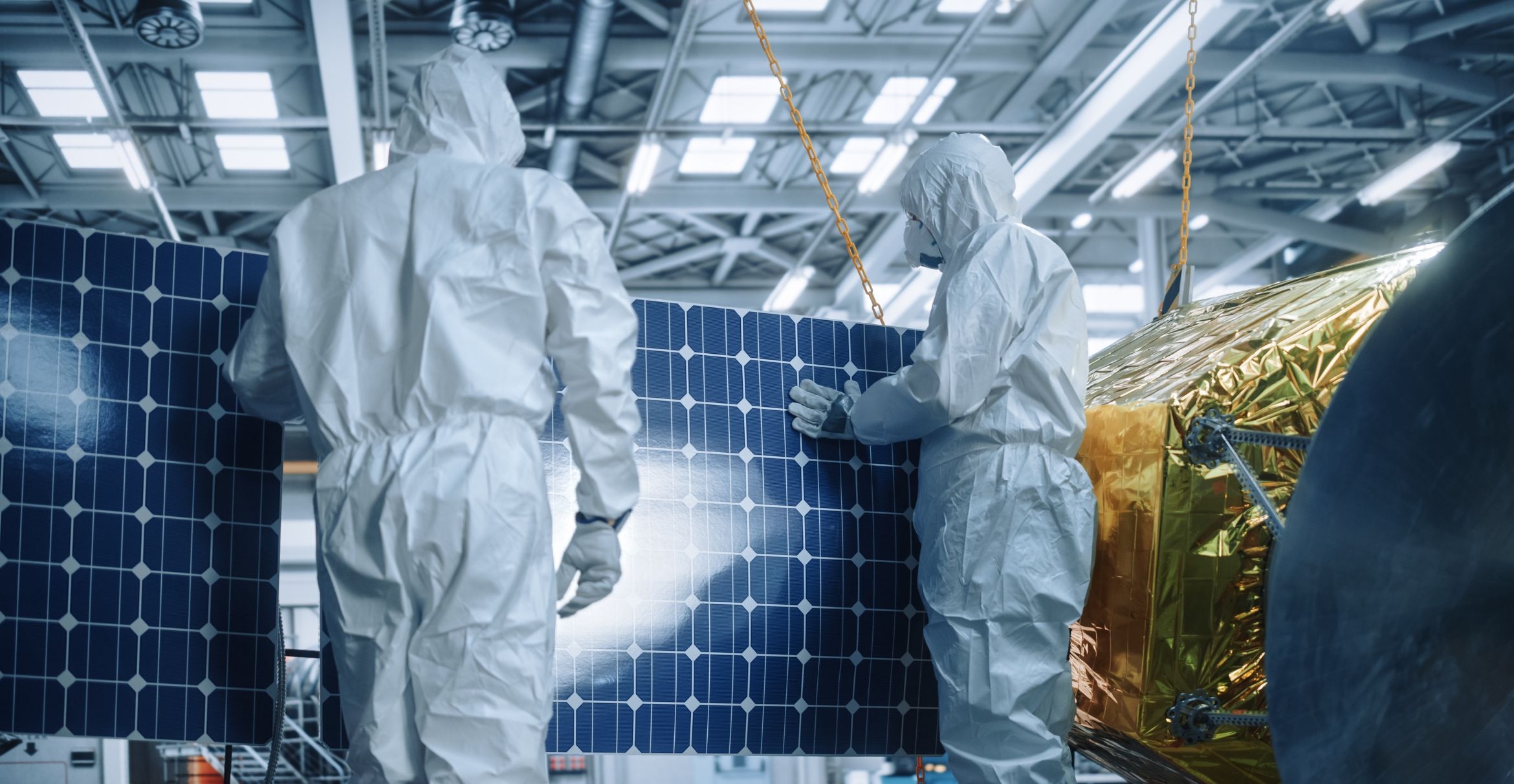 Two workers in white coveralls and masks examine solar cells in a cleanroom.