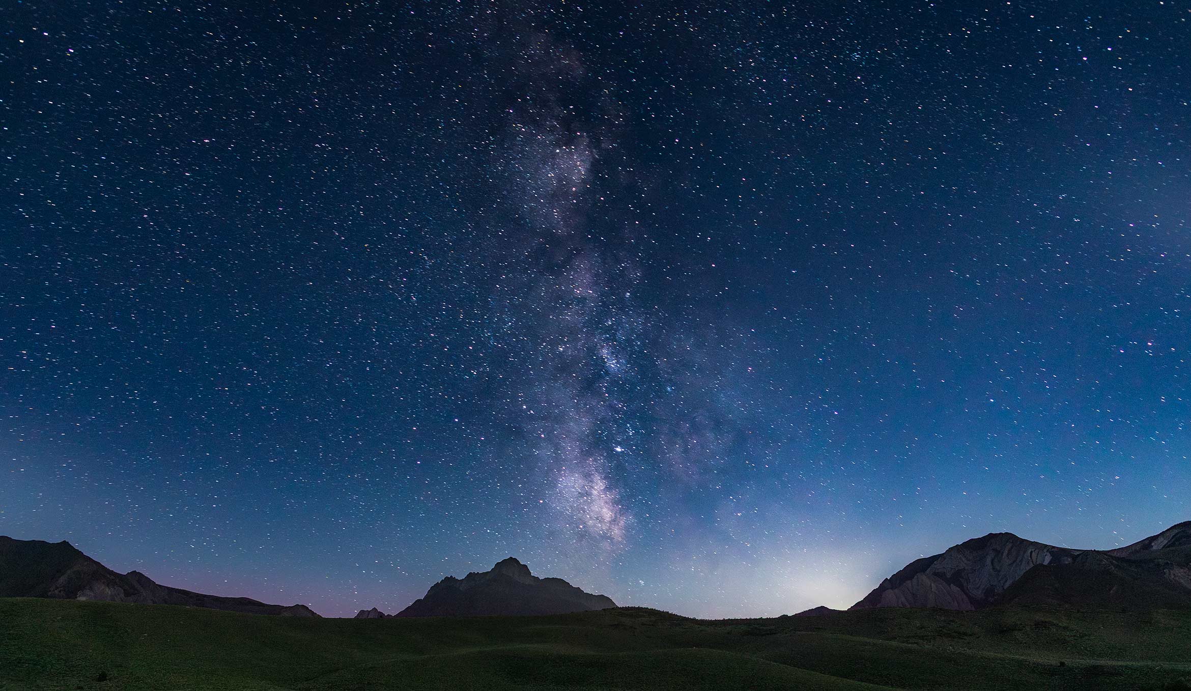 a night sky full of stars and Milky Way above silhouetted mountains