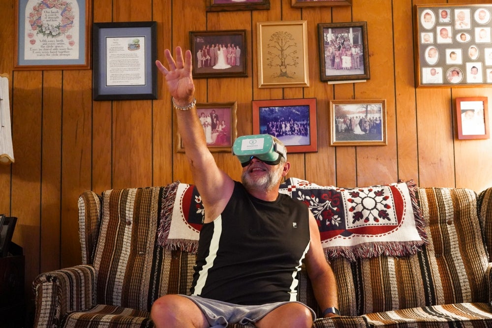 Man with VR goggles sitting on a chough, smiling and reaching for something