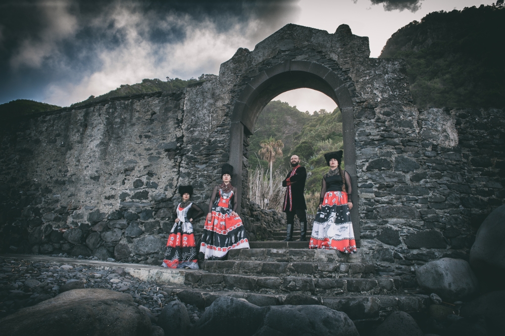 One man and three women in traditional Ukrainian clothes stand under a stone archway with cloudy skies