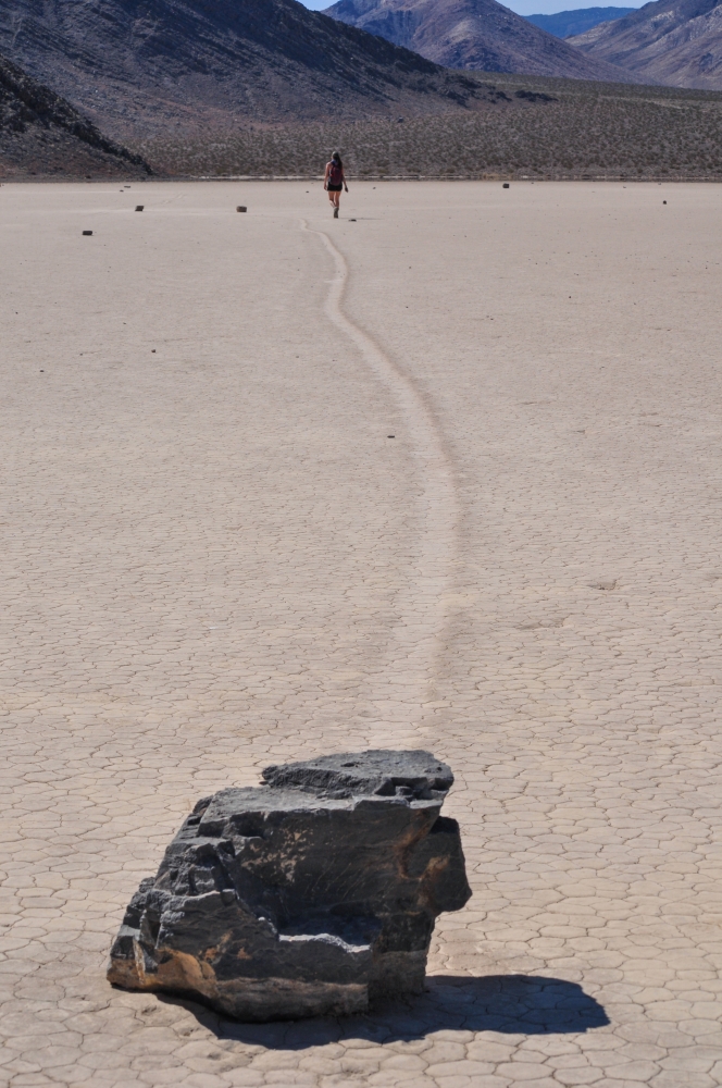 A sailing stone with tracks leading into the background where a person walks toward the distant mountains