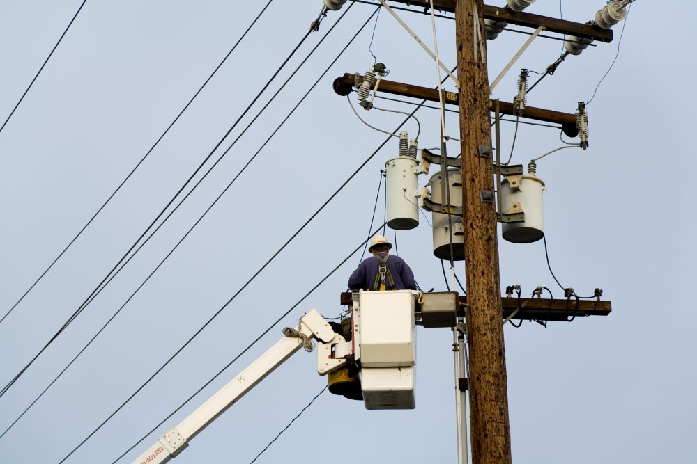 Power company worker wearing a hardhat is repairing electrical wires from a utility bucket truck.