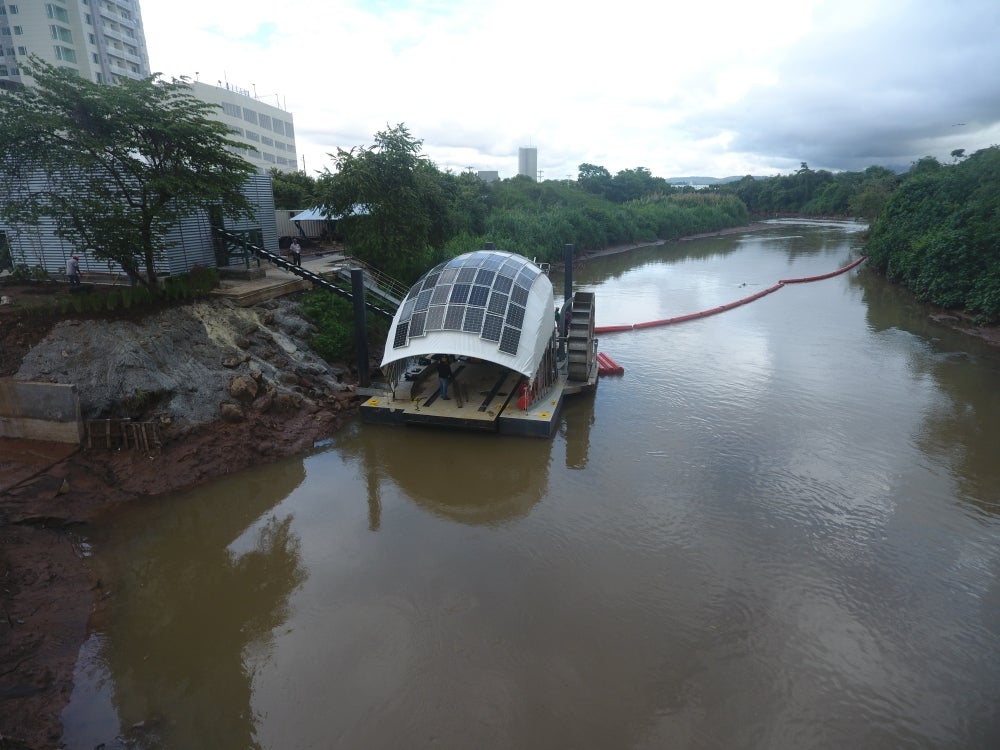 A mechanical wheel topped with a tarp-like cover tiled in solar panels sits in a river