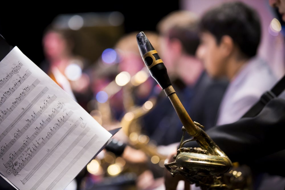 music sheet and wind instrument in foreground with musicians playing in background