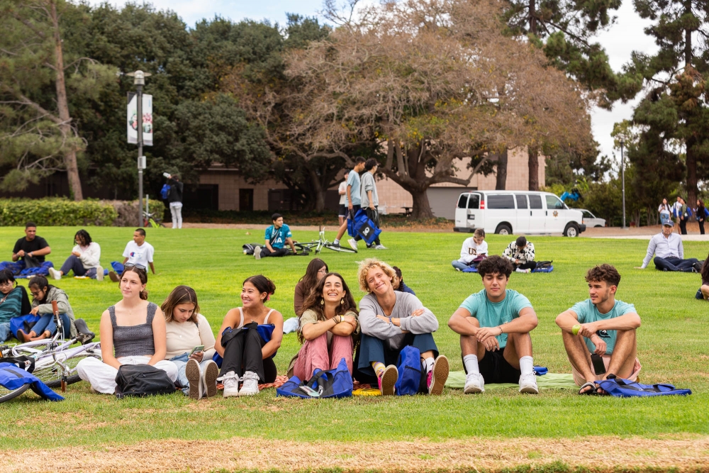 Students sit in a row on green lawn