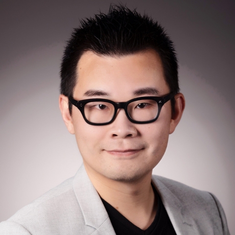 William Wang smiles for a headshot wearing black glasses and a suit