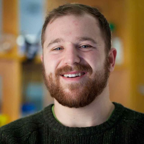 Max Wilson stands in a lab, smiling, wearing a dark sweater