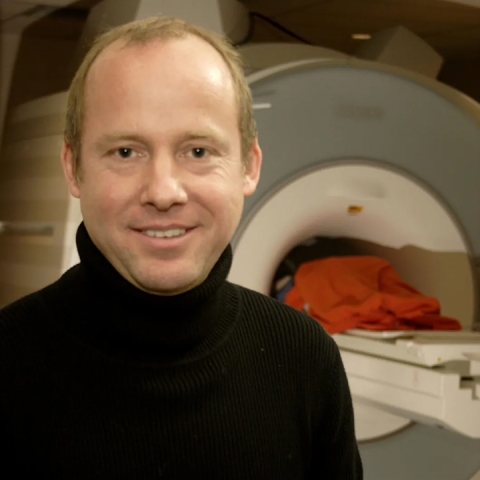 René Weber in a black turtleneck stands in front of an MRI machine