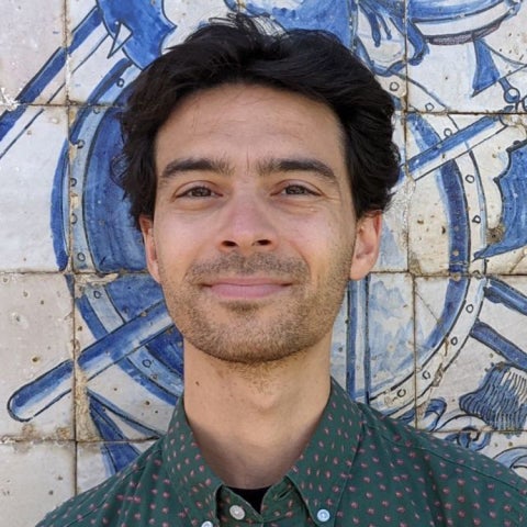 David Caratelli stands in front of a painted wall, wearing a dotted collared shirt