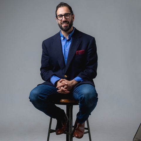 Masoud Movahed sits on a stool wearing a dark blazer over a blue shirt