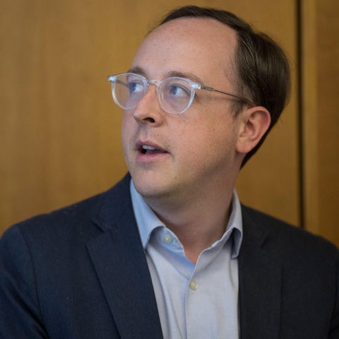 Matto Mildenberger looks to the left, wearing a suit jacket and blue collared shirt