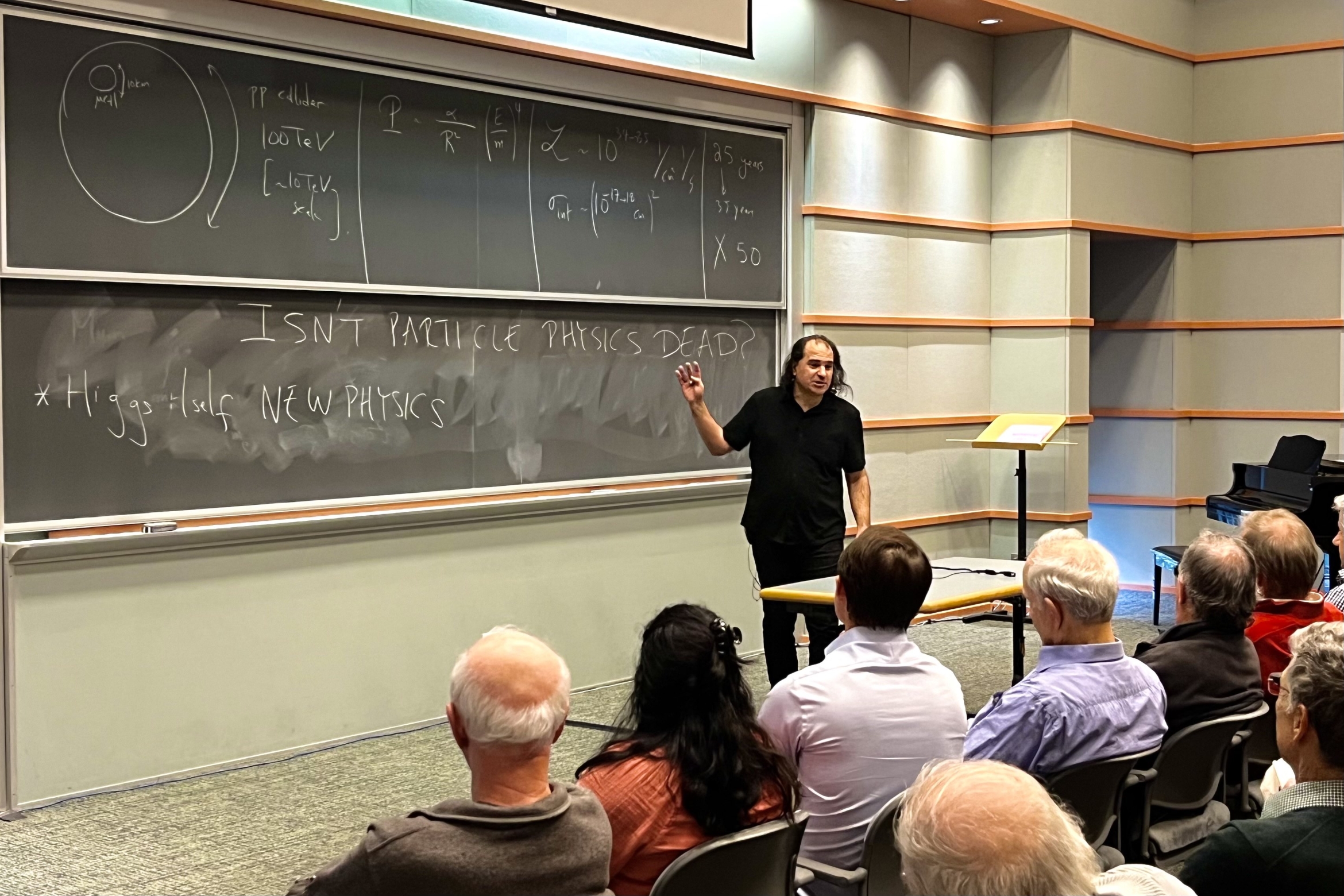 “Particle physics isn’t dead,” reads the blackboard behind an expressive physicist presenting to a packed audience.