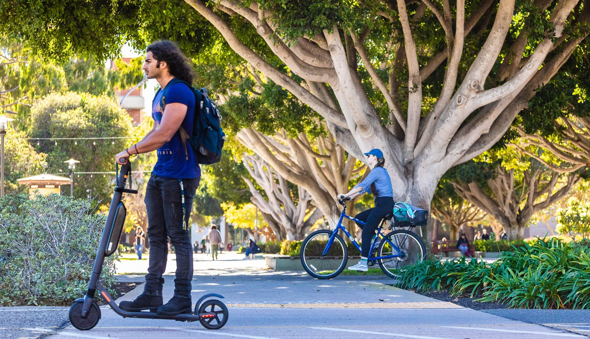 Students riding bikes and scooters with trees in the background