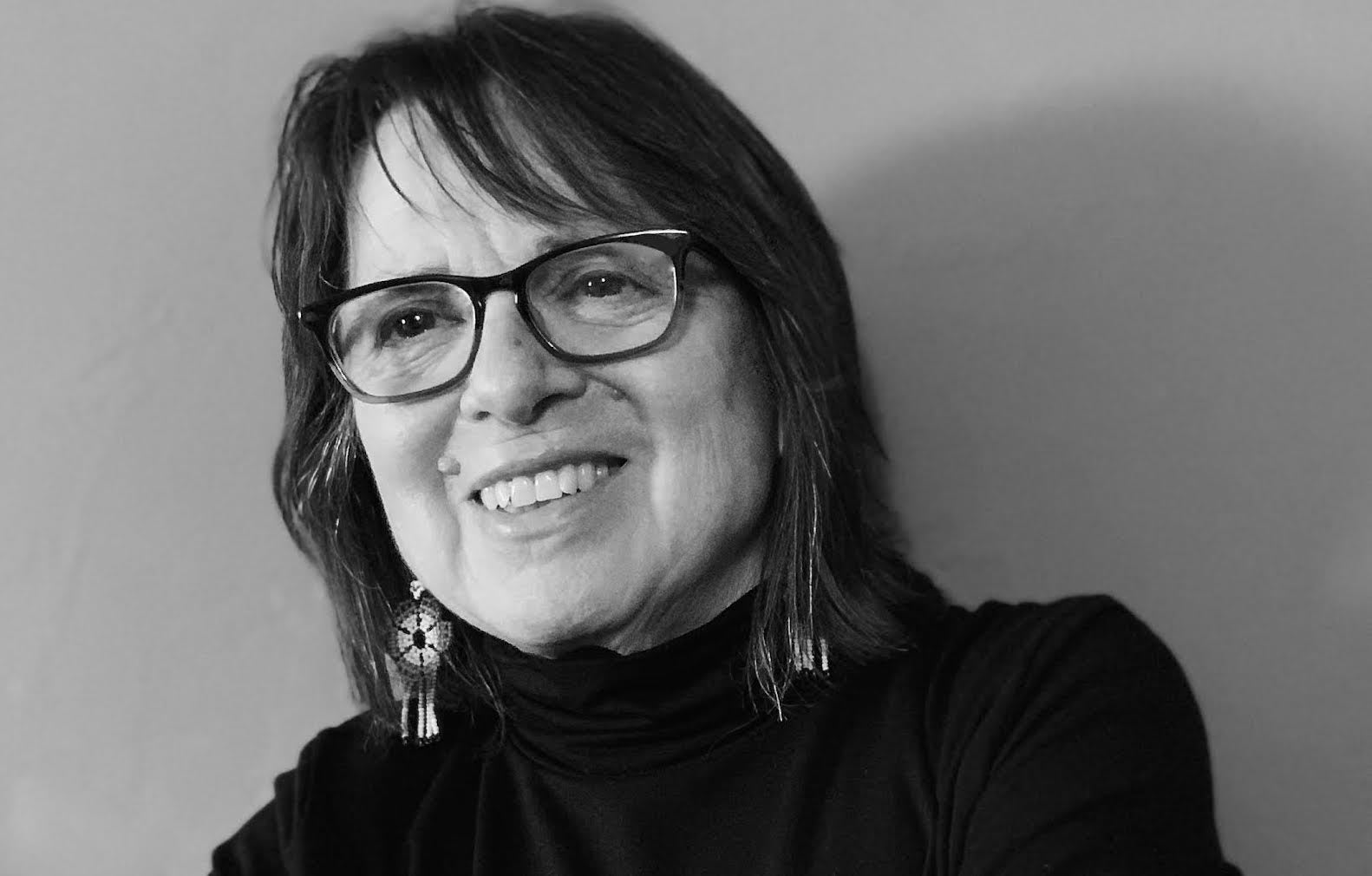 Cherríe Moraga wearing a black turtleneck and black rimmed glasses