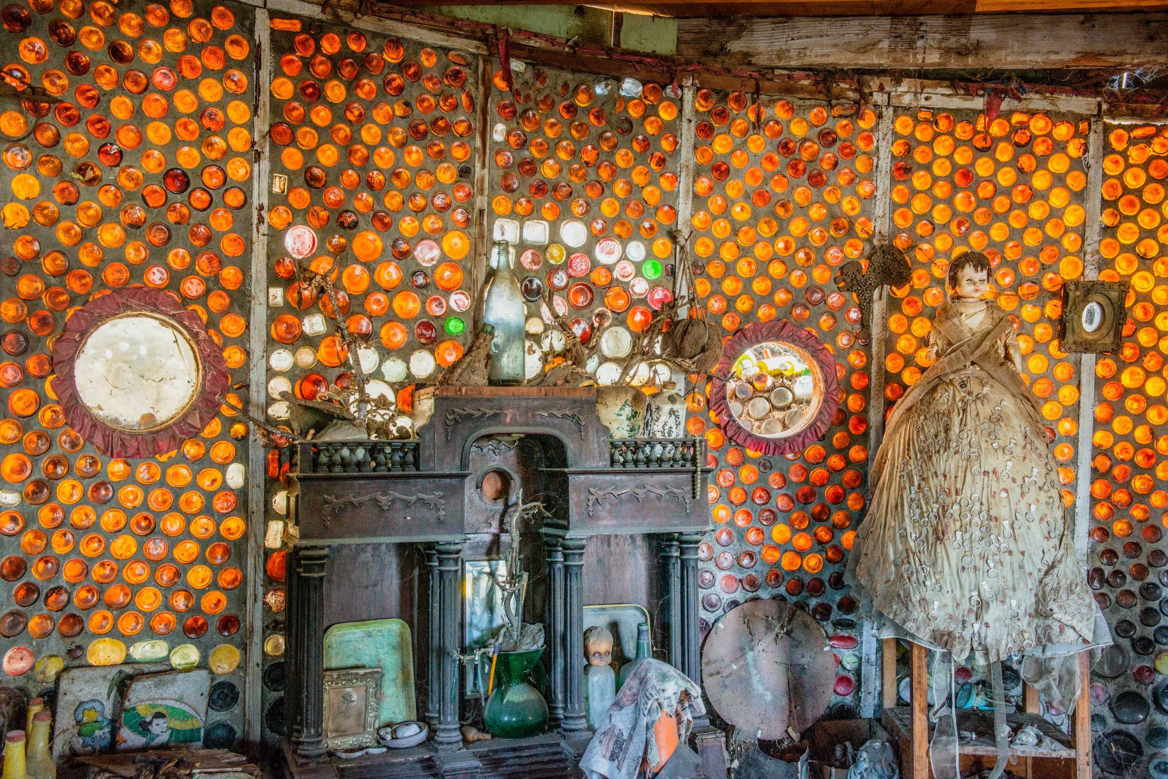 Orange glass bottle mosaic structure with dolls and miscellanea 