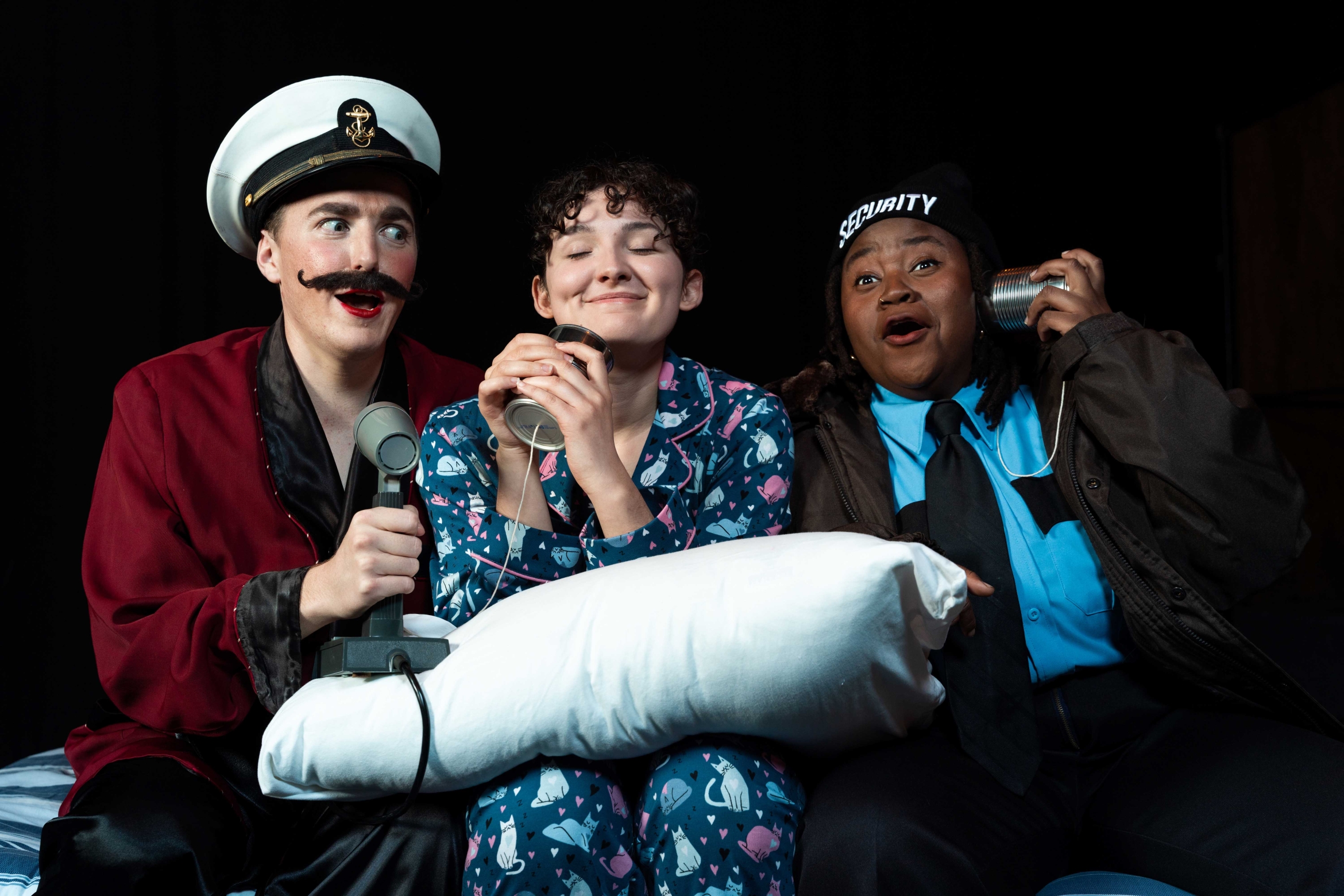 Three actors on stage, one in a sea captain's hat, one in pajamas, one dressed as a security guard