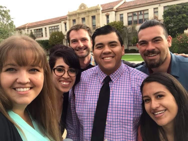 A diverse group of adults in professional attire standing outside a school, smiling