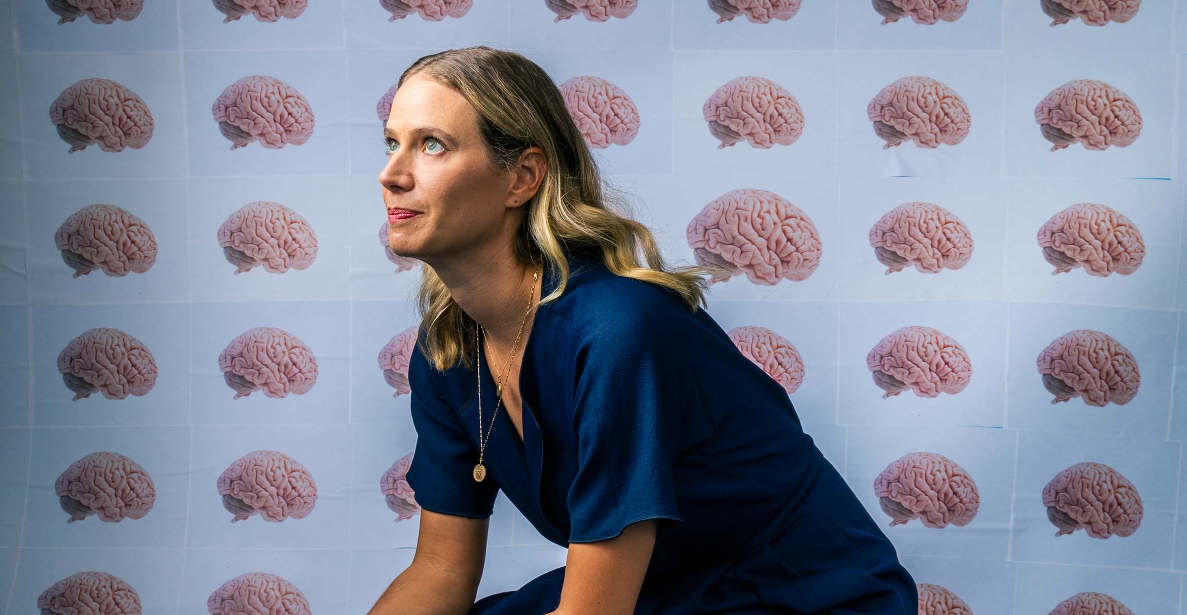 Emily Jacobs seated, looking upward, seated in front of a backdrop of brain imagery