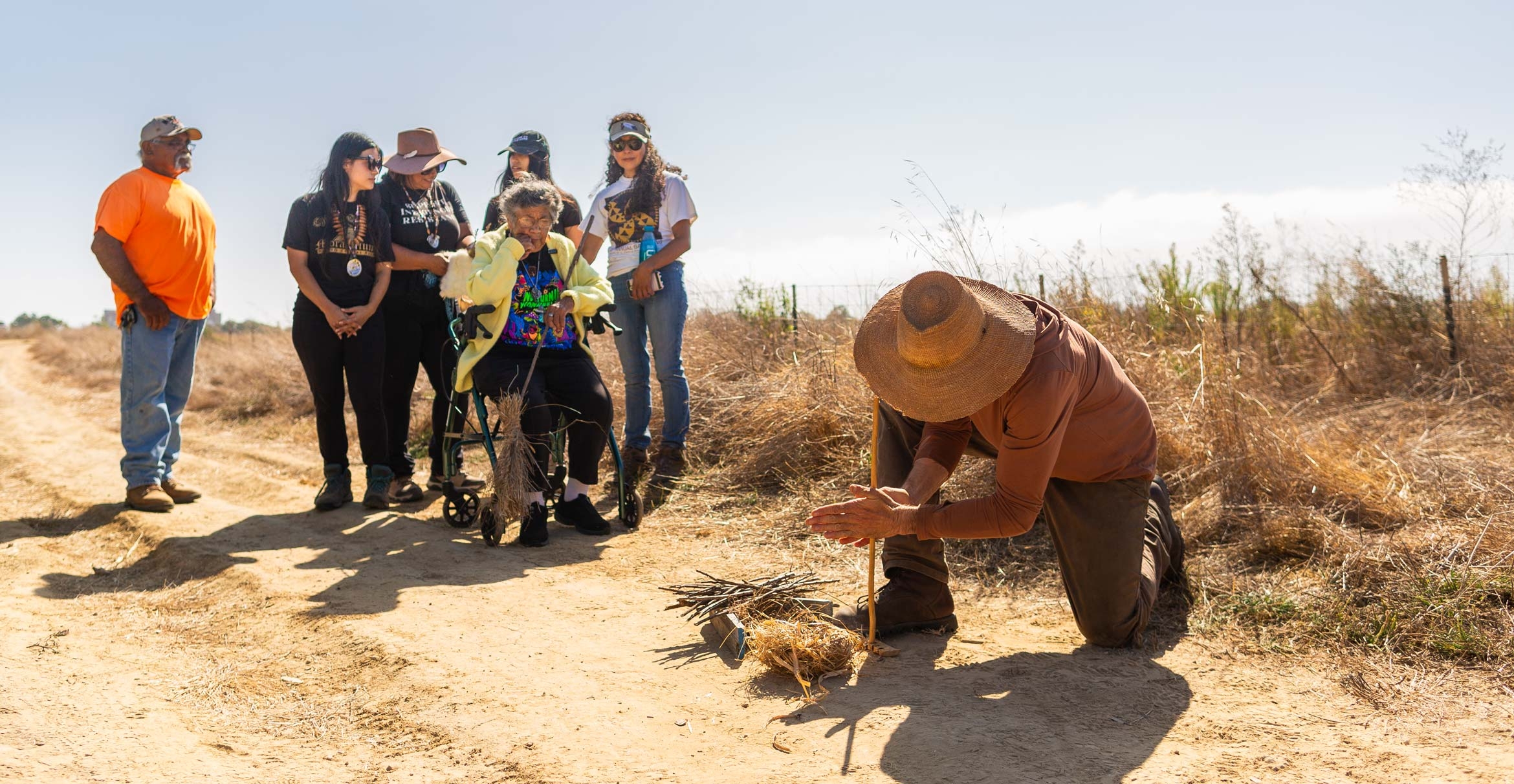 Wayne Chapman uses a hand drill to start a coal, which Chumash Elder Ernestine Ygnacio-De Soto (seated) will use to start the fire.