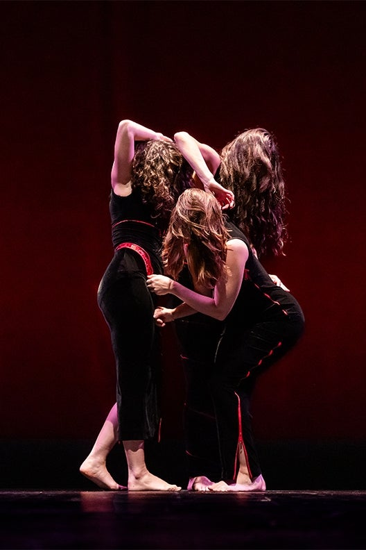 Three female dancers entwined on a dark stage