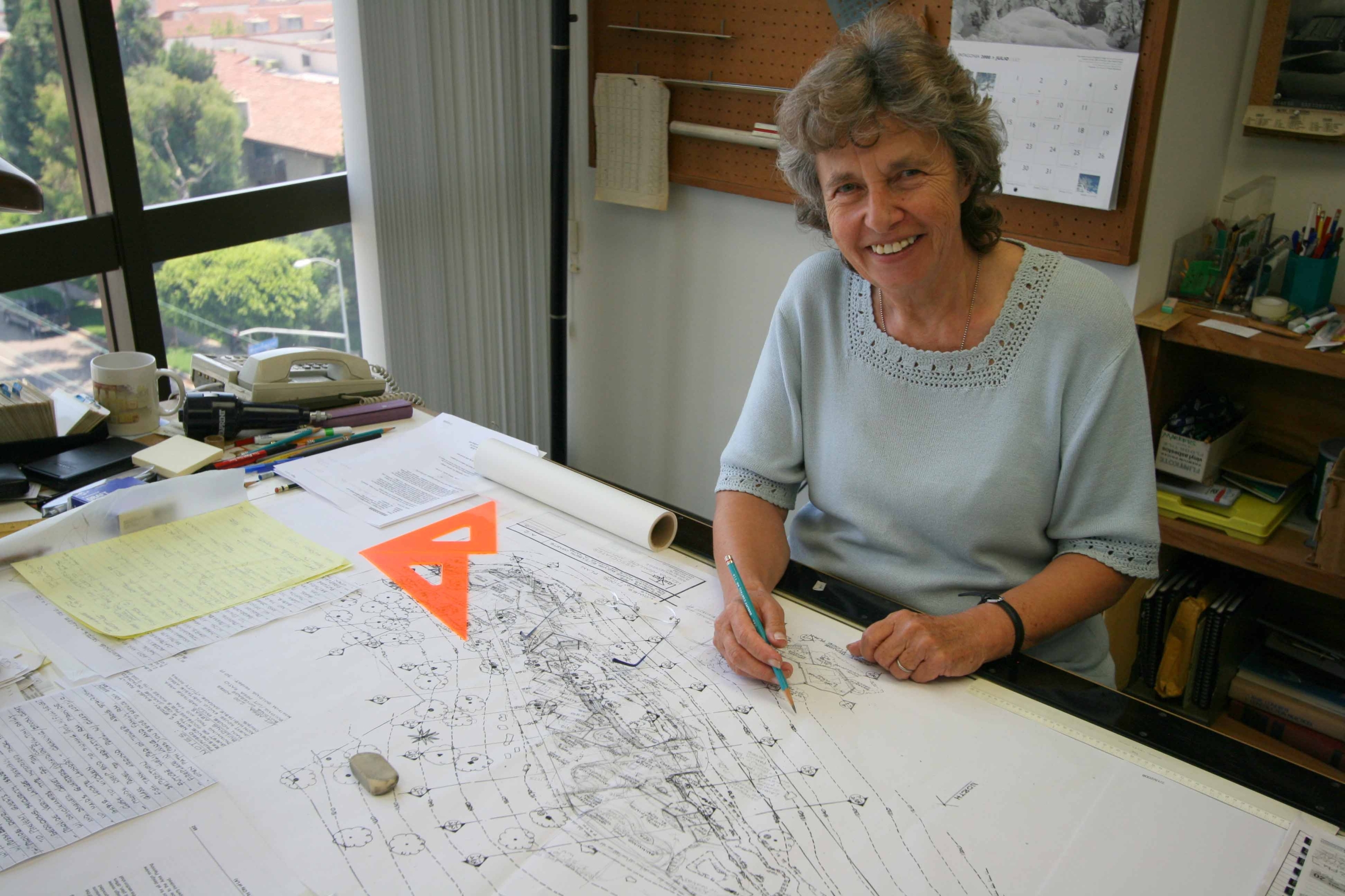 Woman with grey hair at desk with architectural drawings
