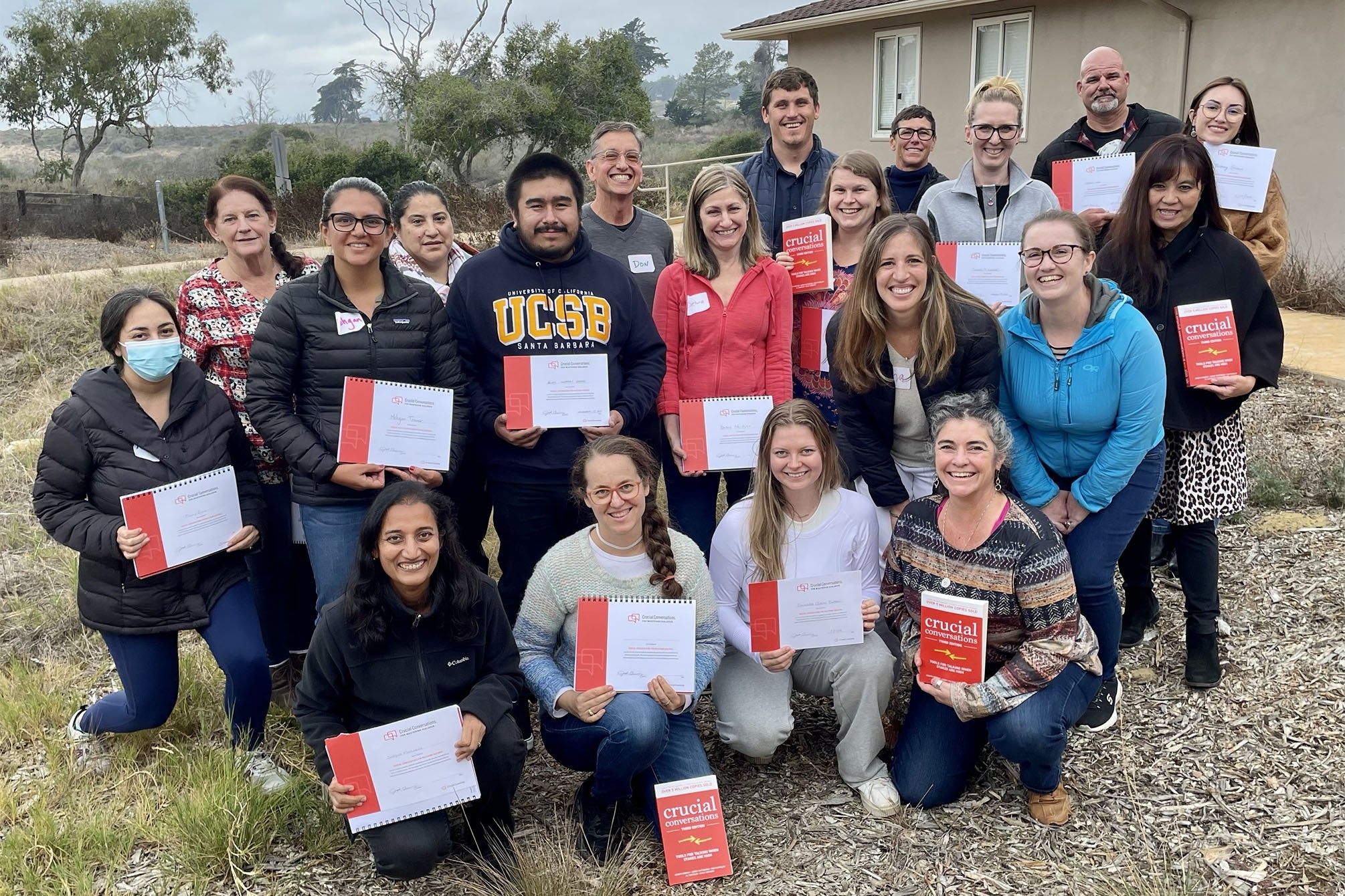 A diverse group of adults outside, holding certificates of completion and smiling