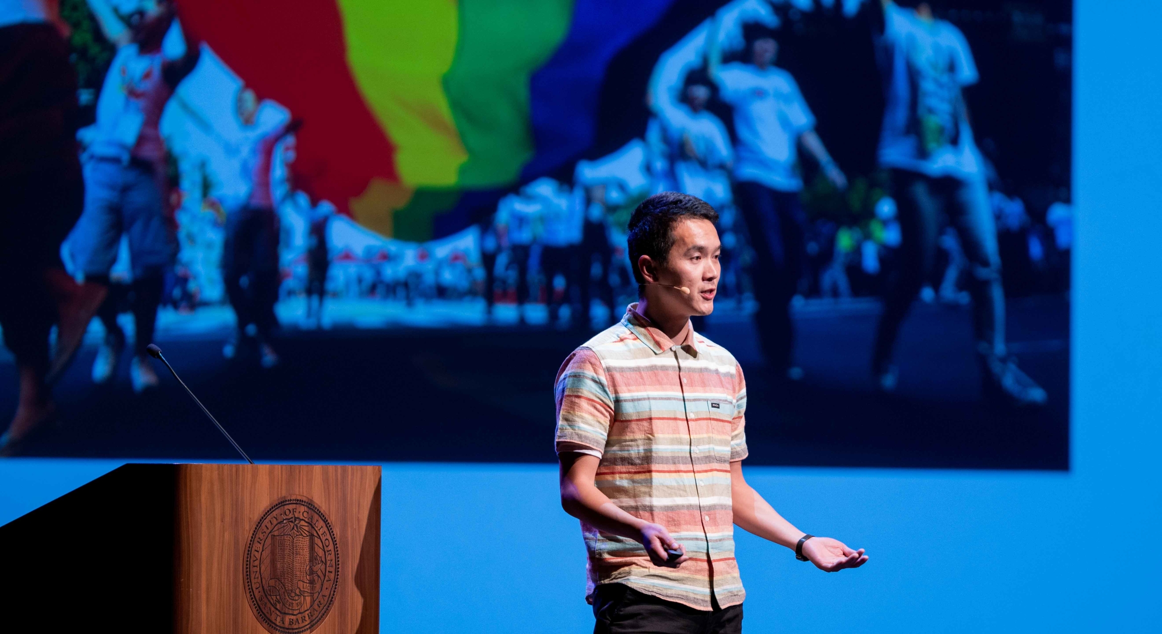 an Asian man stands next to a podium speaking on stage