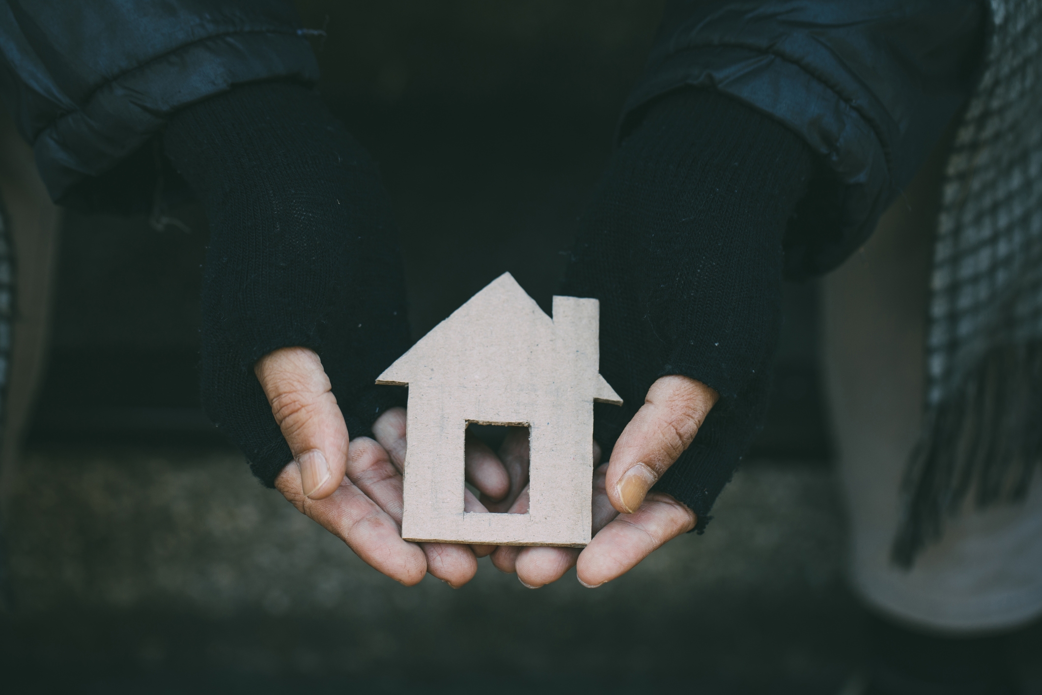 Two hands in fingerless gloves hold a cardboard house