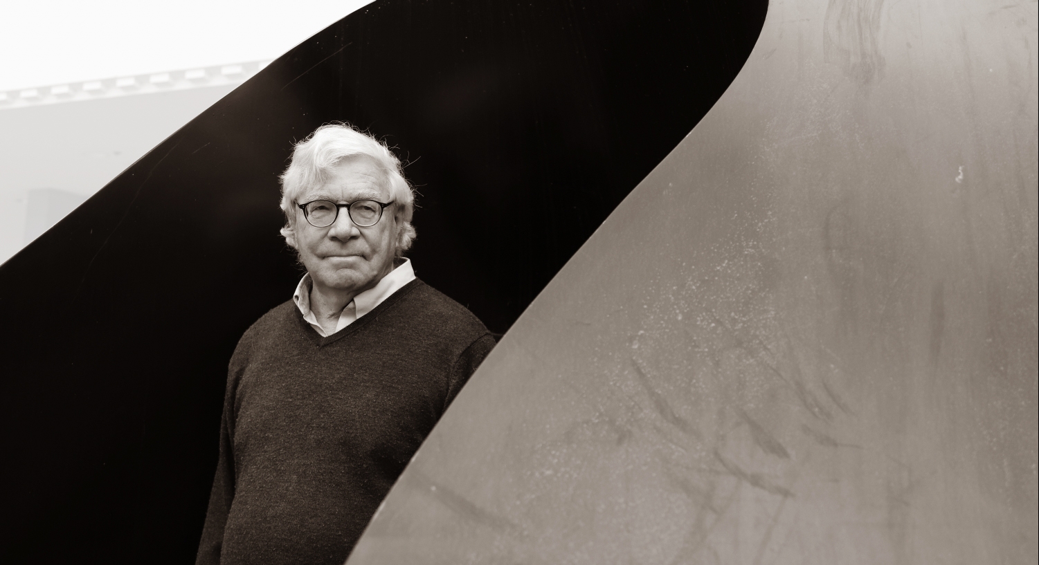 man in sweater with grey white hair inside a black sculpture's shadow