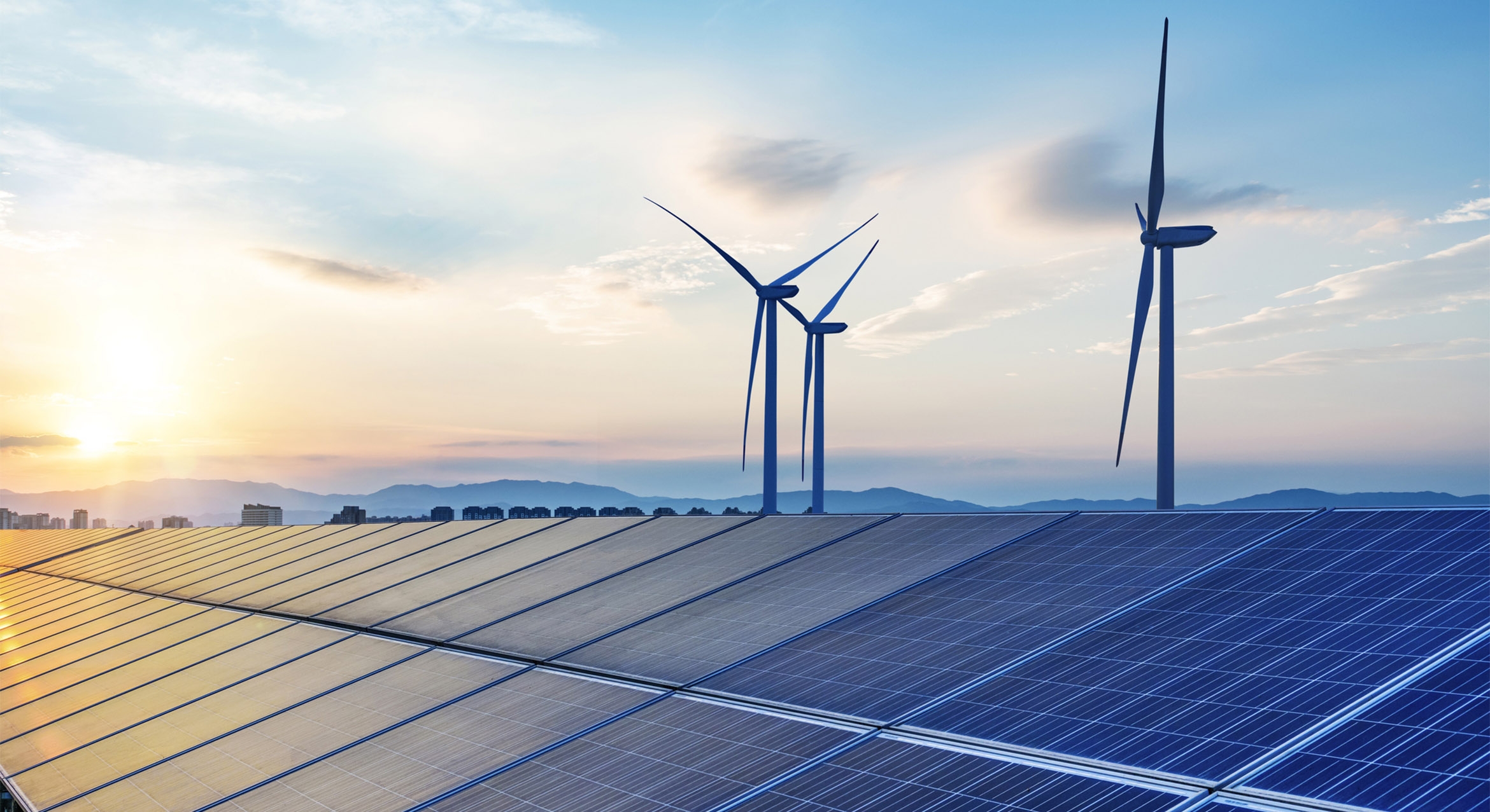 Wind turbines behind solar panels at sunset