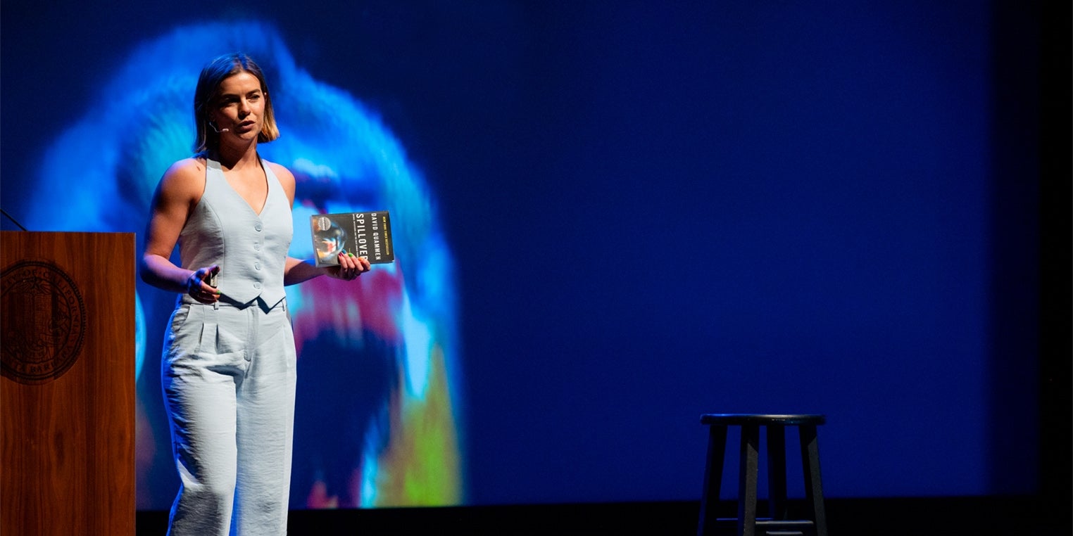 A woman in a suit speaking from a darkened stage