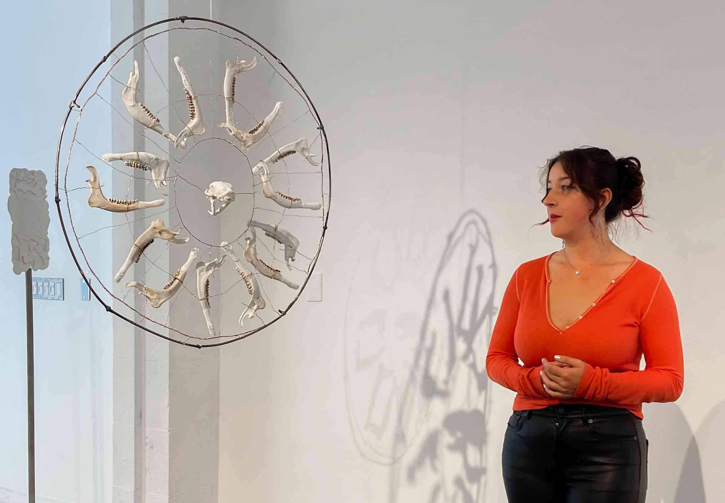 white woman in orange shirt with hanging sculpture