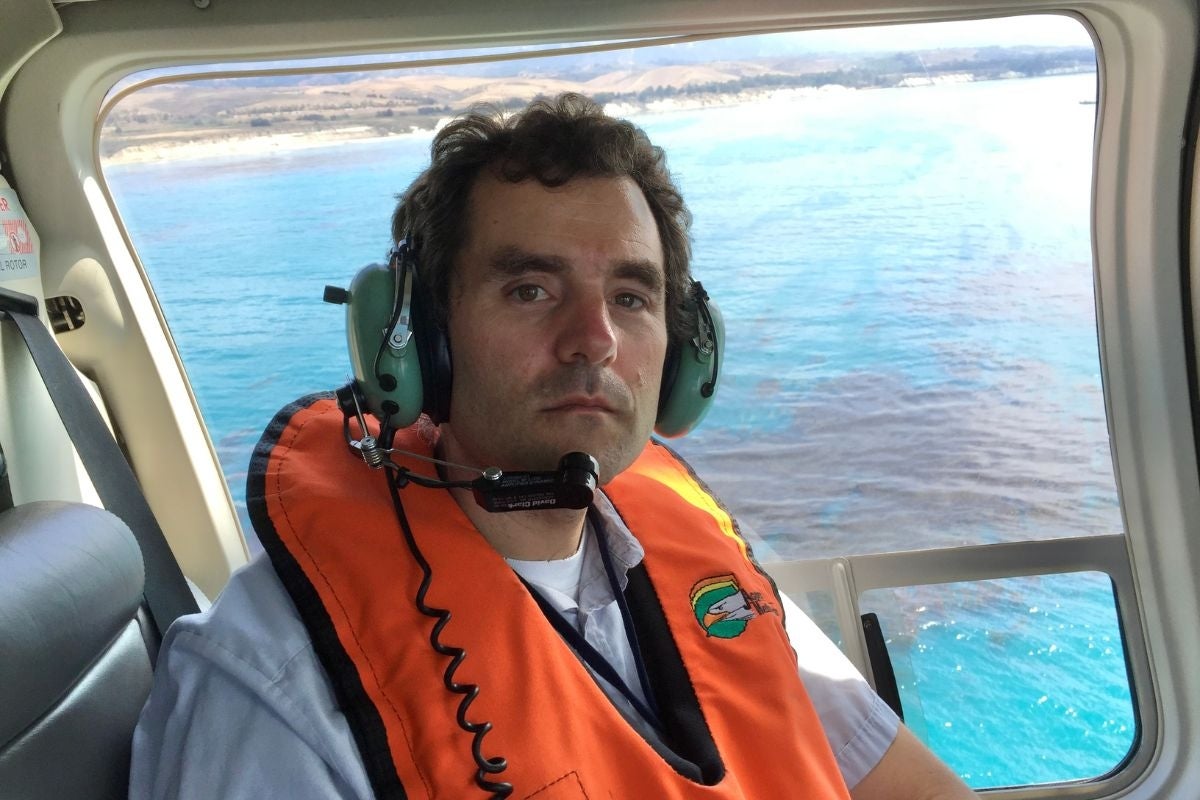 David Valentine sits in a helicopter with oil visible in the seawater below.