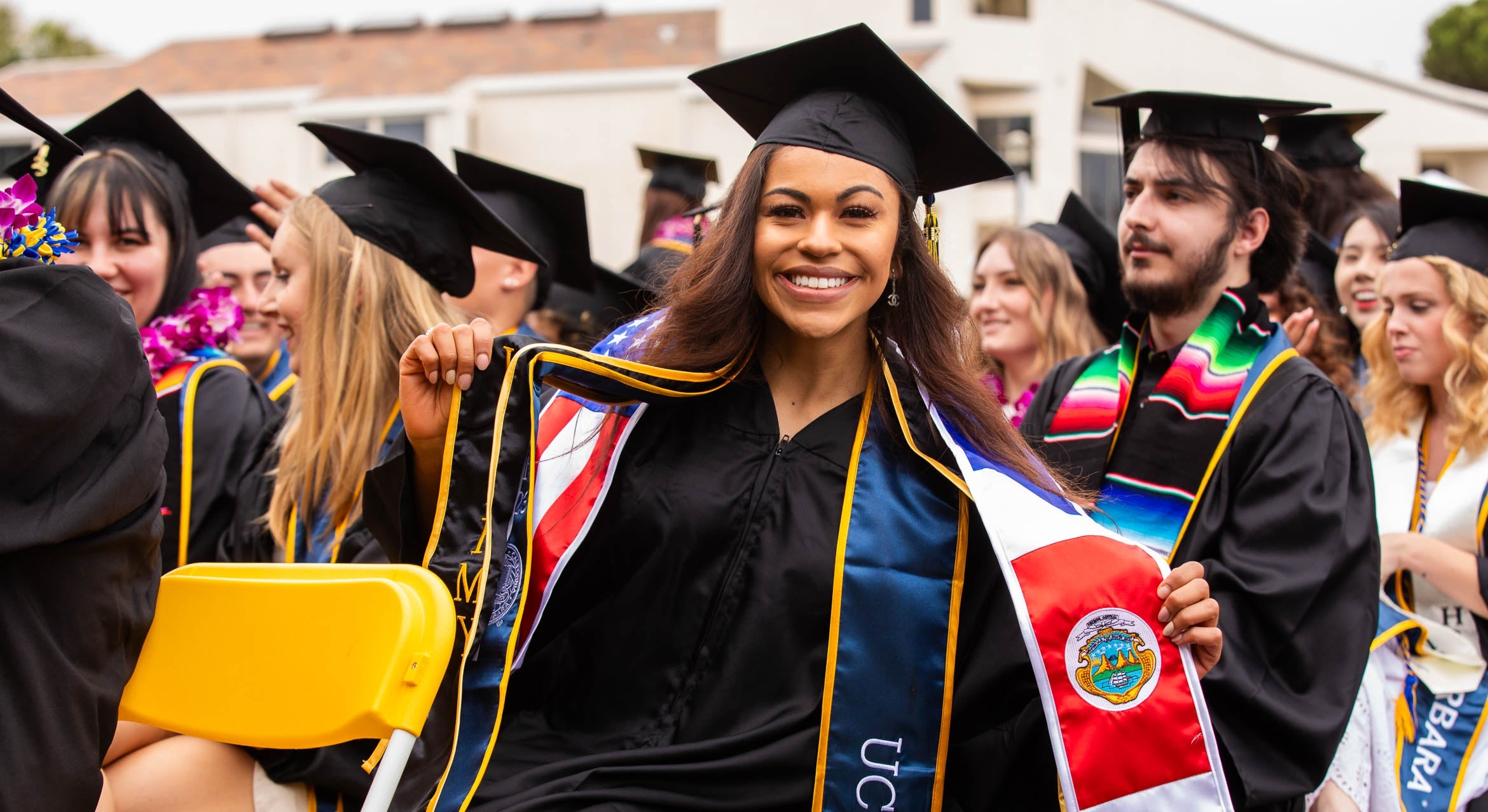 A smiling graduate holds up a sash