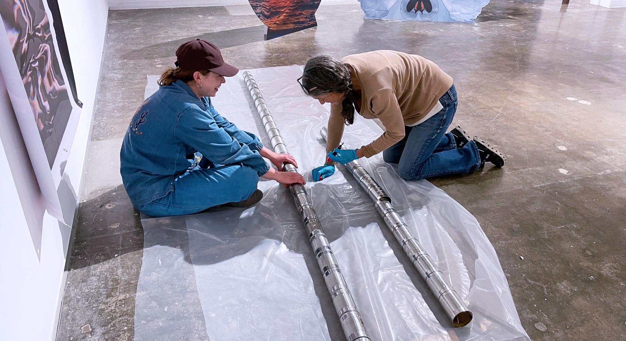 two women on gallery floor with dozens of cans