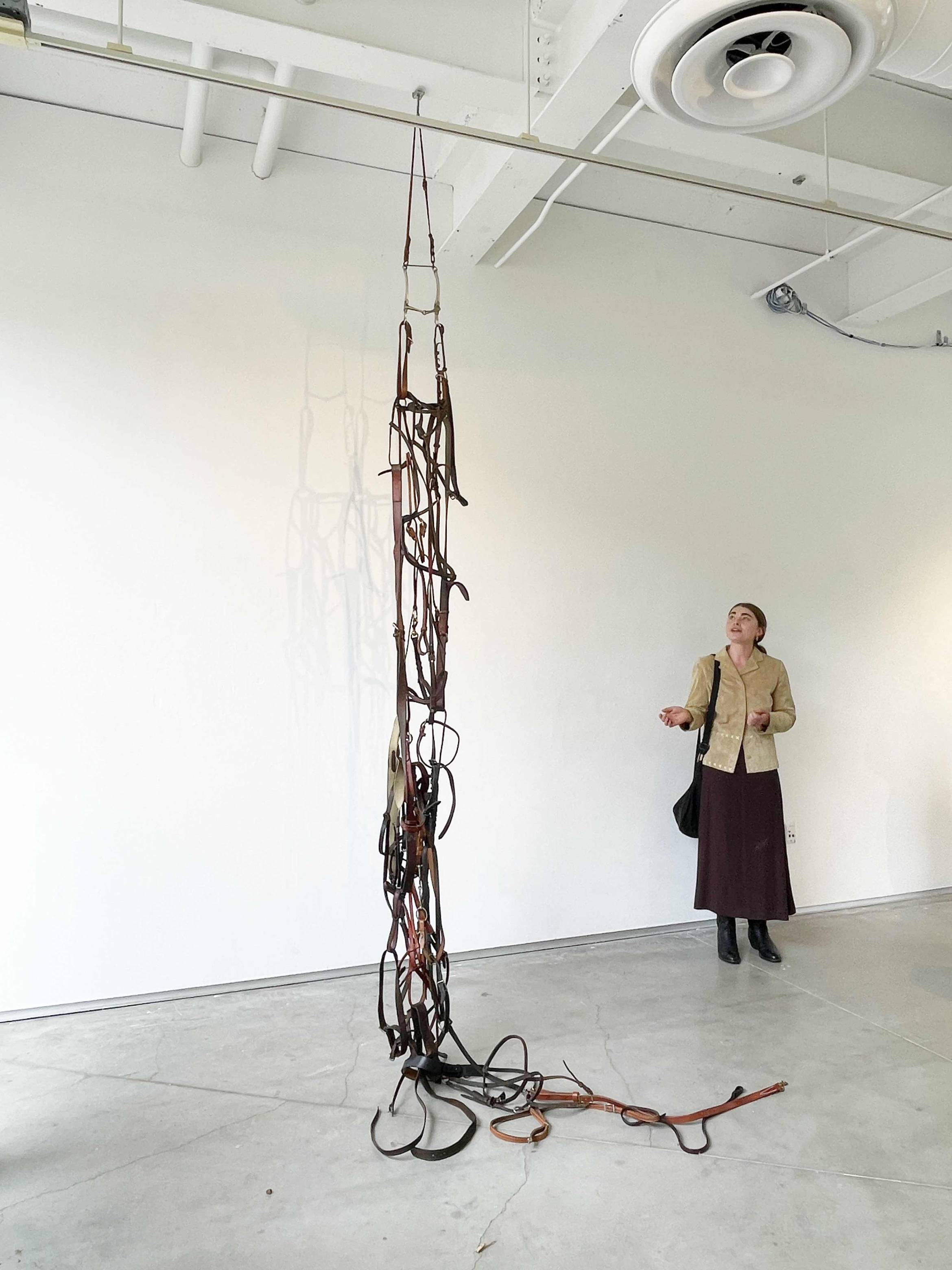 women standing beside gesticulating presumably talking about the large sculpture of knotted leather bits hanging from the ceiling