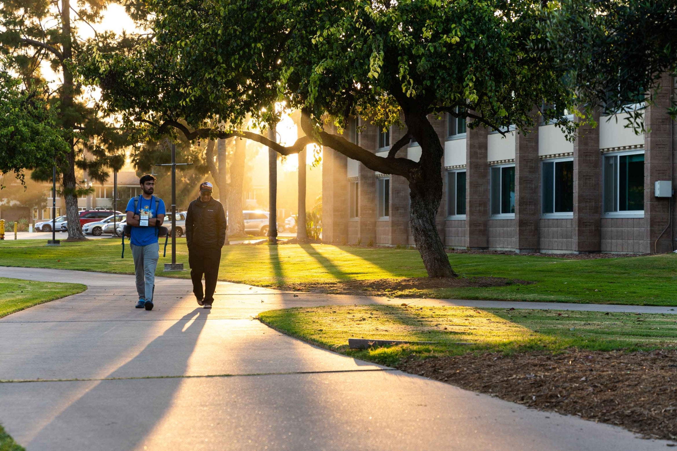 two men walk at dusk with building and trees