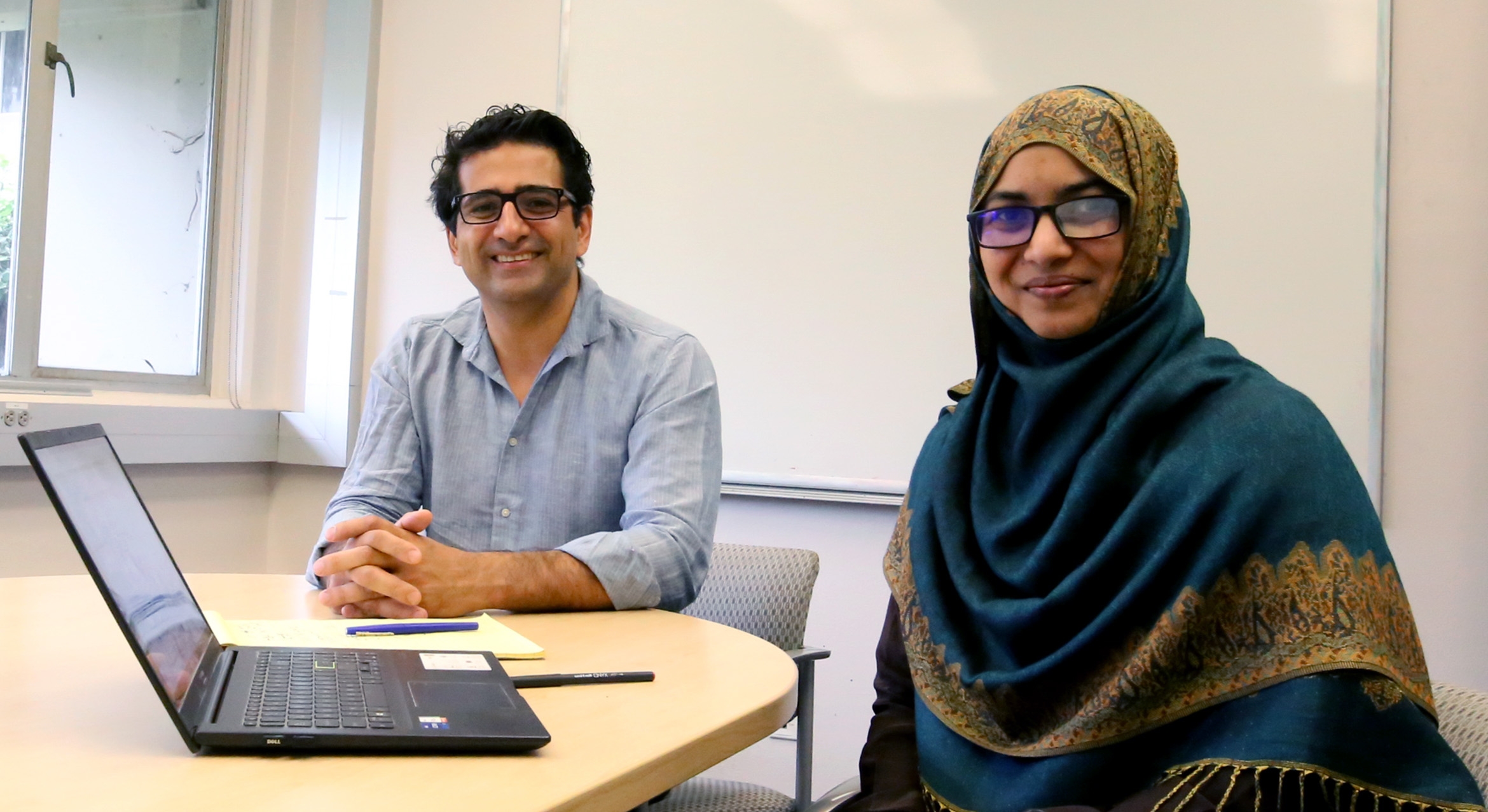 man with glasses and woman in hijab at table with laptop