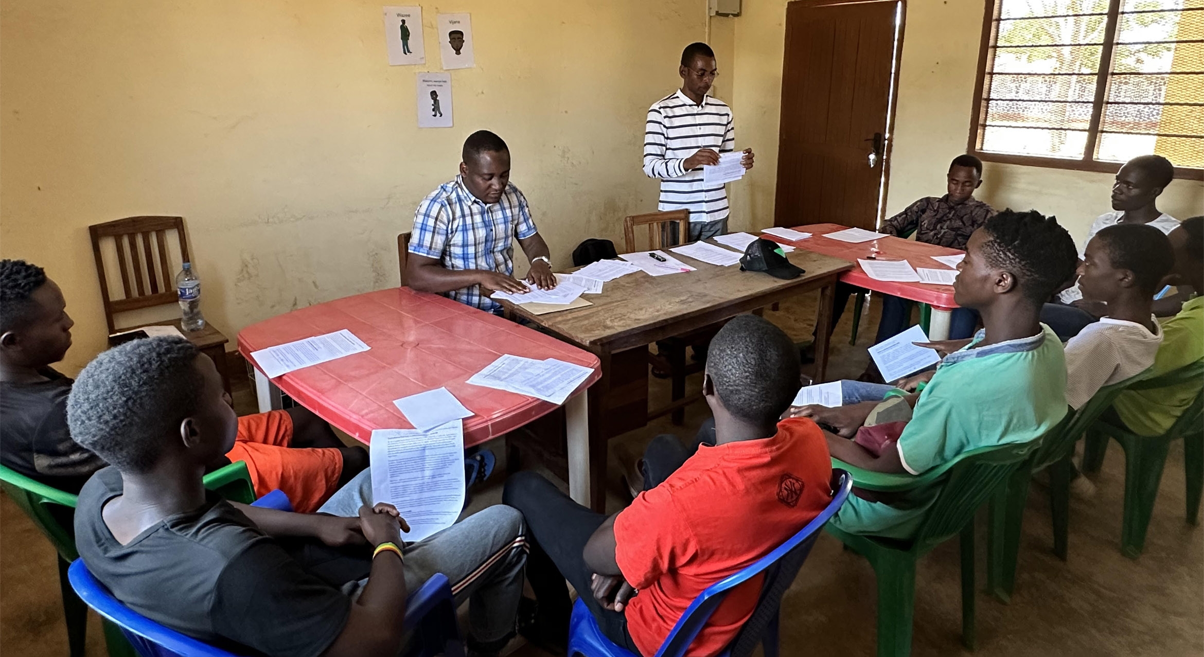 a group of Tanzanian men gather around a table and speak with a researcher