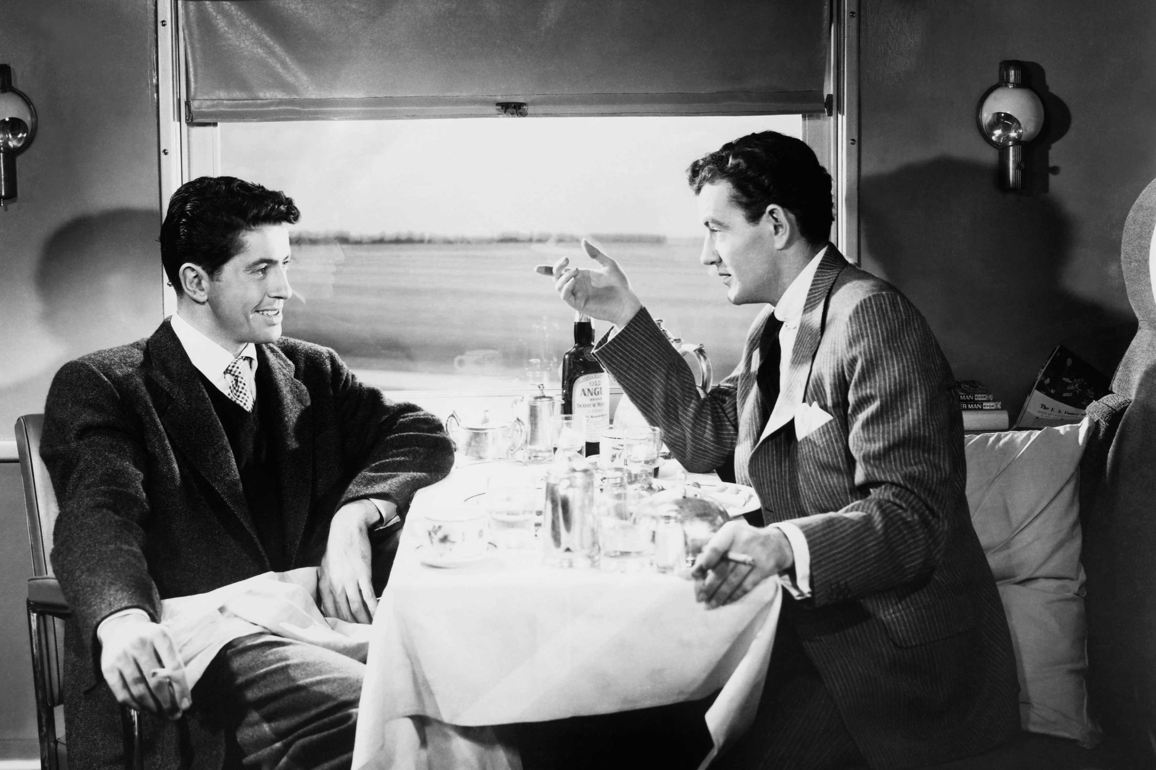 black and white image of two men talking on a train