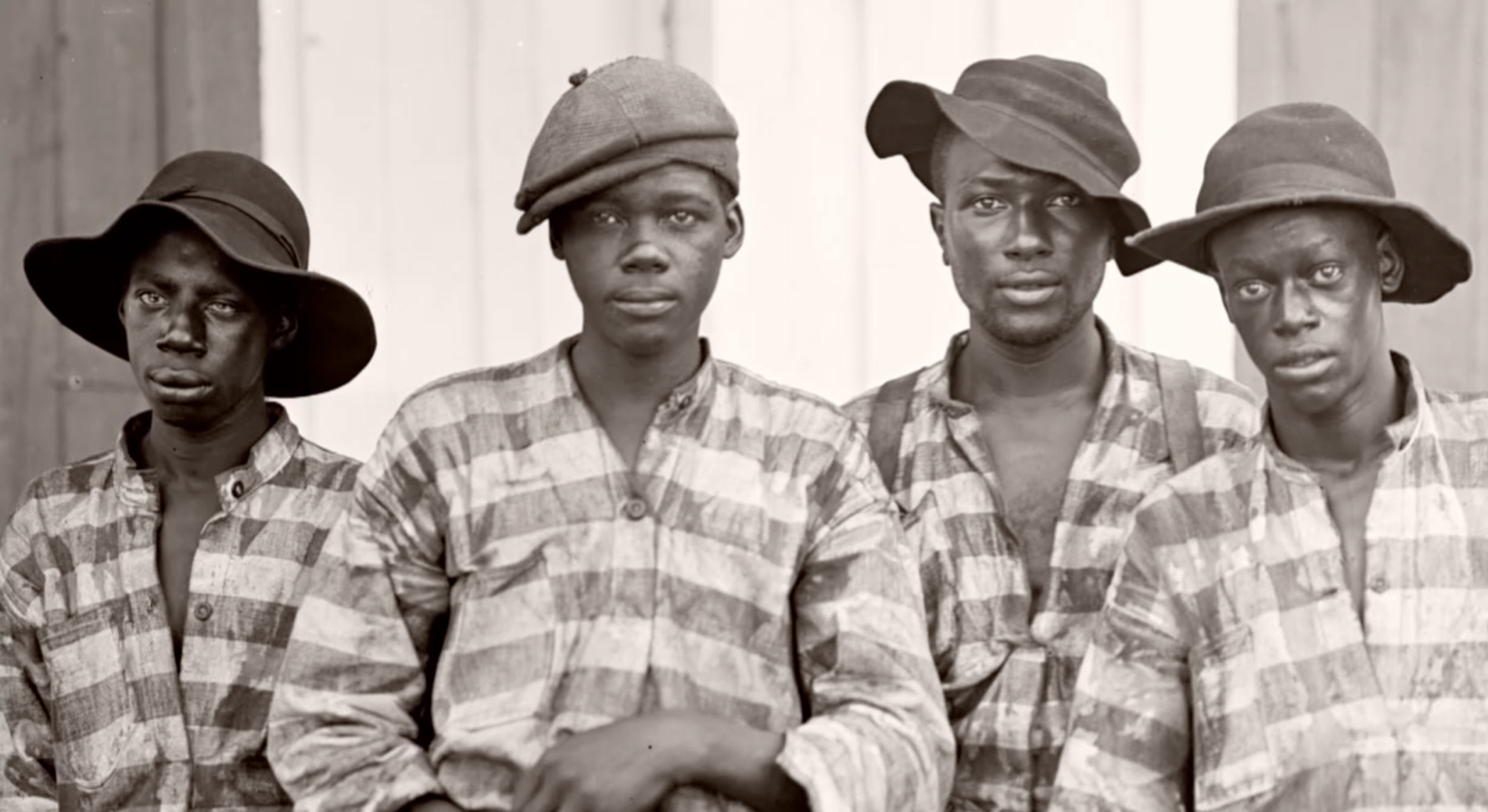 black and white photo of four african american men wearing striped prison uniforms in the late 1800s 