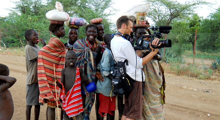 white man holding camera with many people behind him who are Black