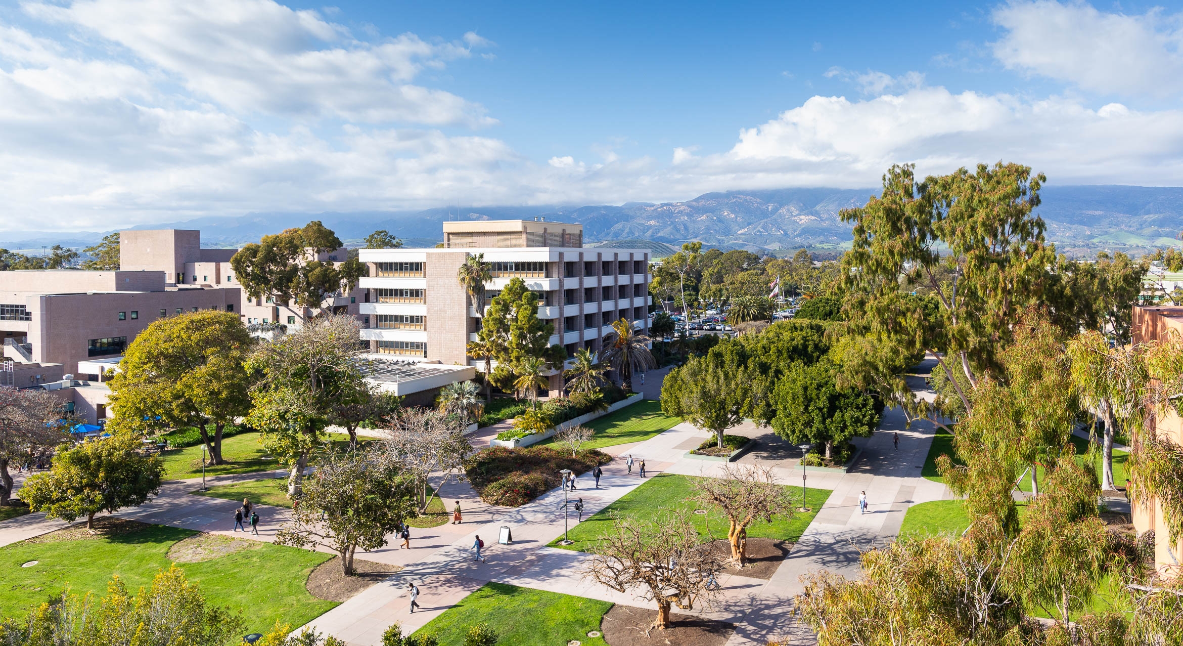 Aerial view of university buildings surrounded by greenery with mountains in the background