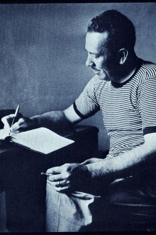 black and white photograph of John Steinbeck sitting at a desk writing