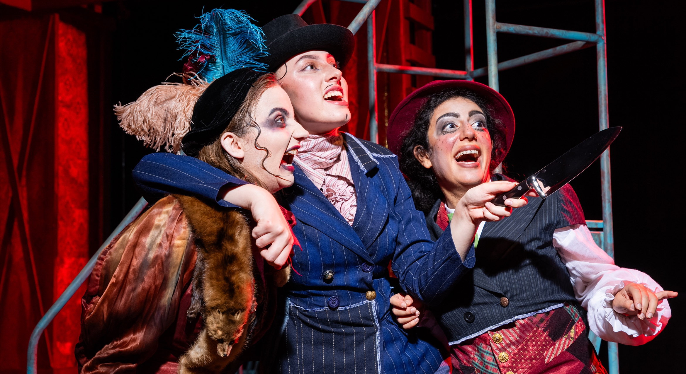 Three actors on a stage in colorful makeup and costumes for The Threepenny Opera