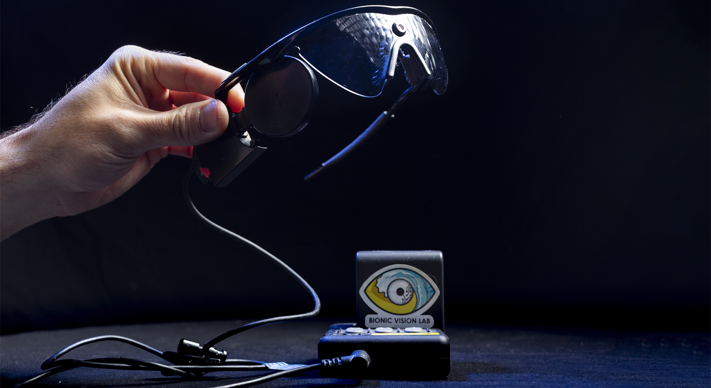 A hand holding up a pair of high-tech glasses on a black background