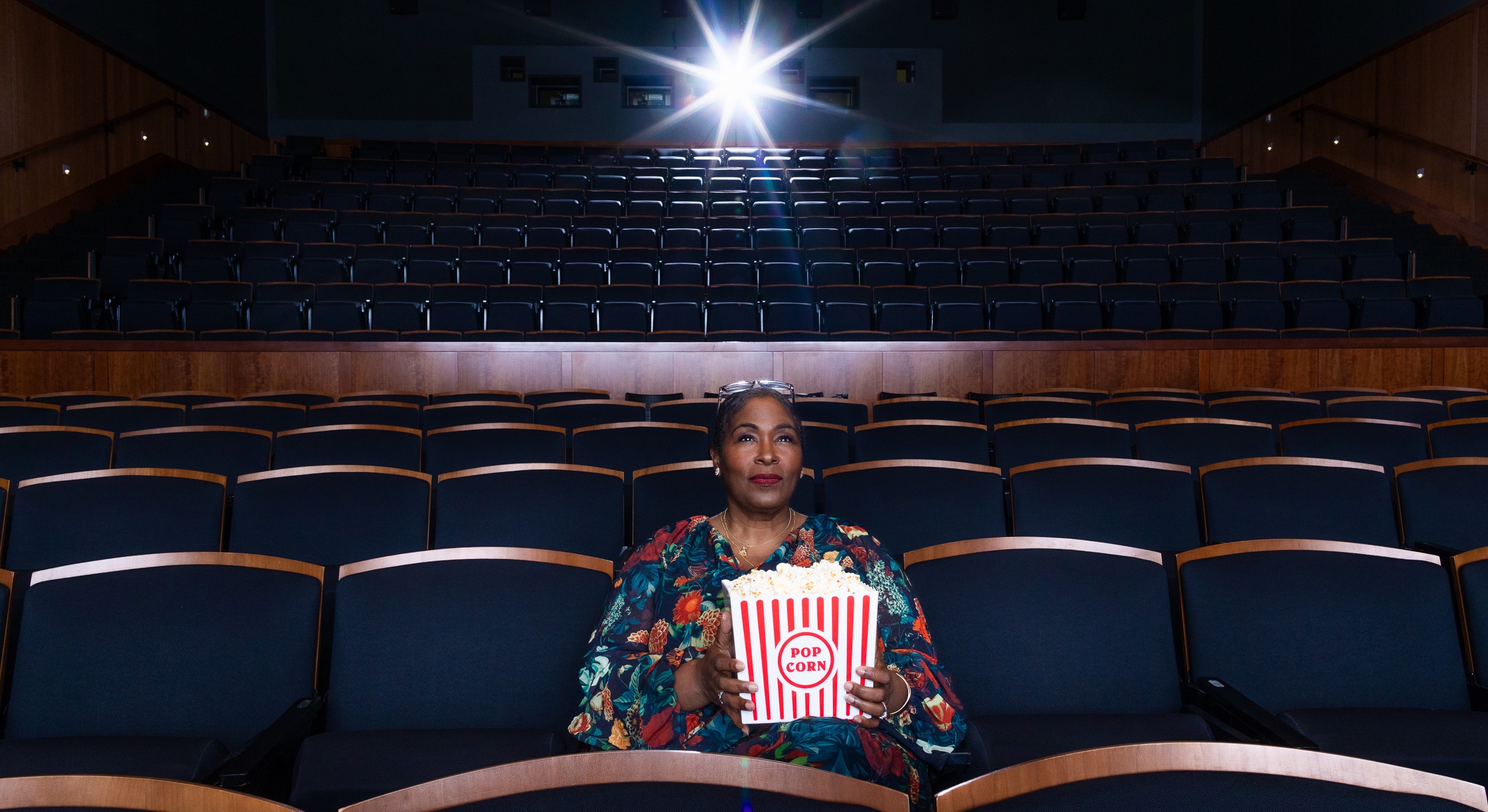 Beautiful Black woman sitting in a dark theater with a prop box of popcorn 