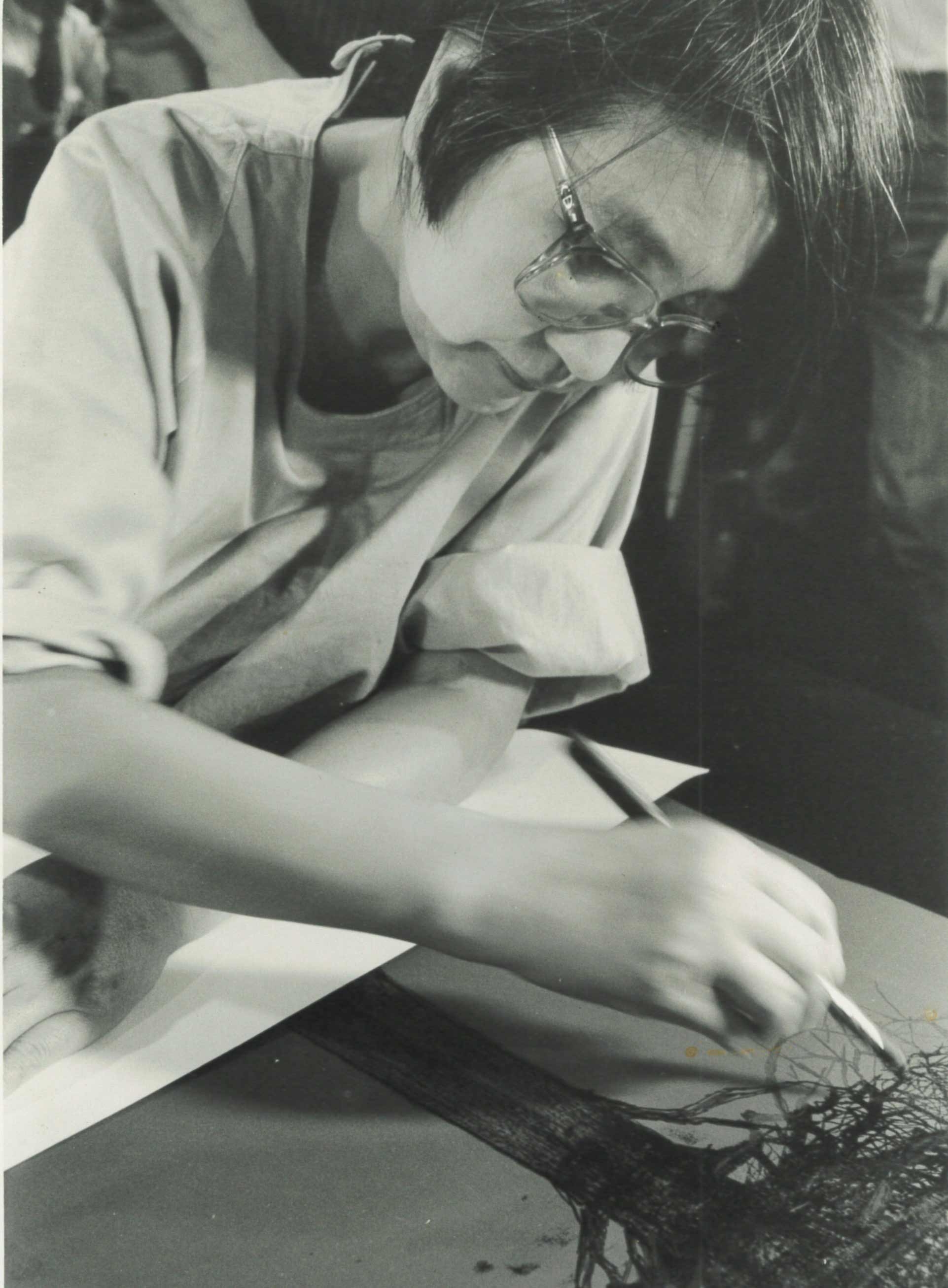 Black and white photo of Japanese artist Taeko Tomiyama as a middle aged woman swirling paint on paper with a brush