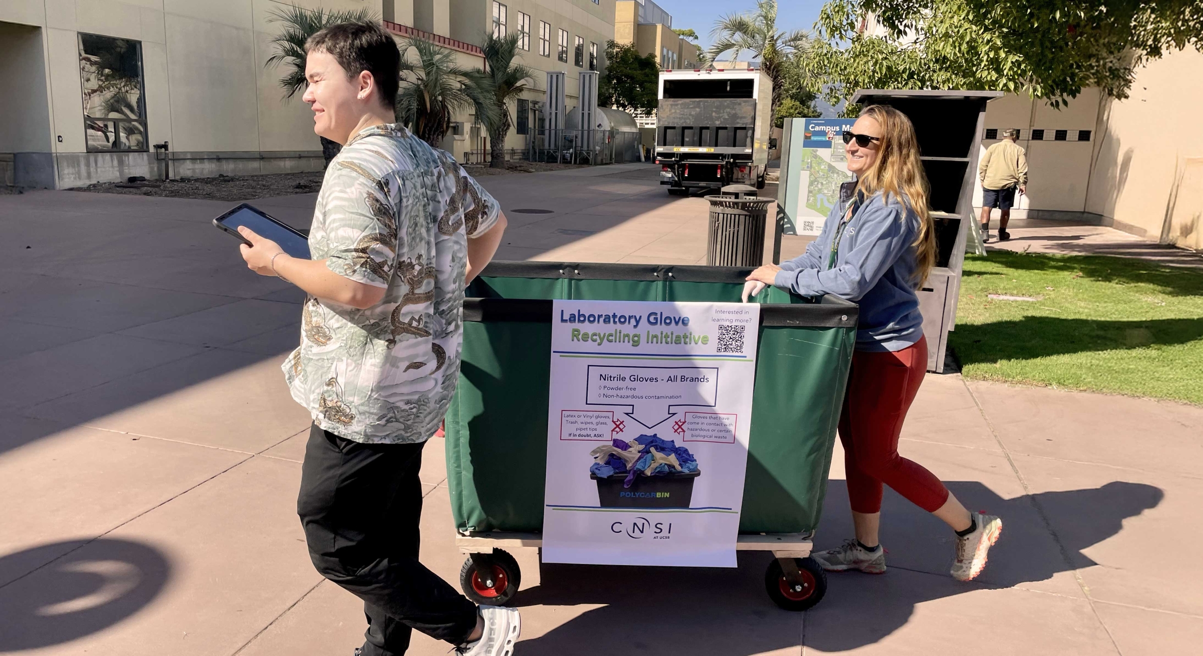 Two adults pushing a cart across a campus