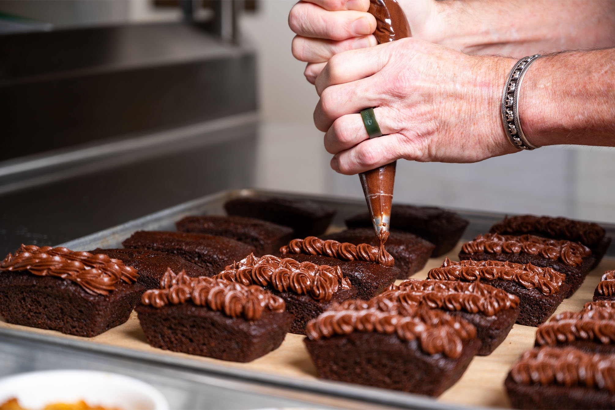 Closeup of hands holding a piping bag and frosting chocolate cakes